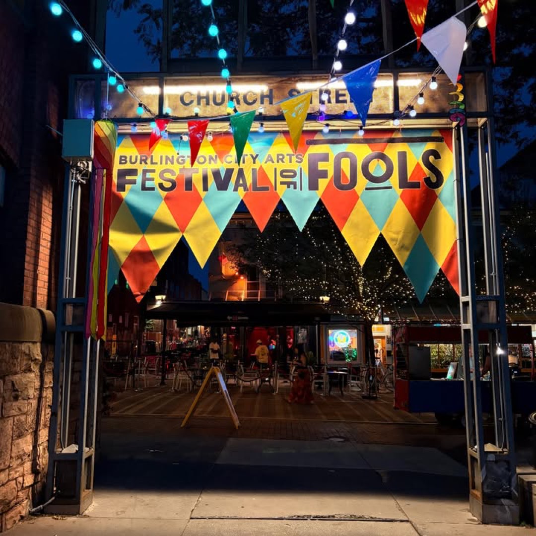 The Festival of Fools banner over Church Street at night, shops lit behind it