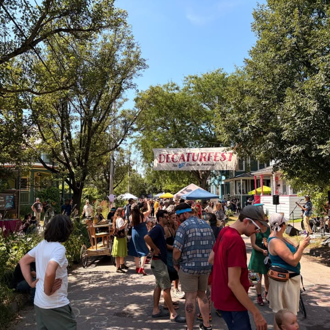A street festival crowd under the trees, tents and a band down the block